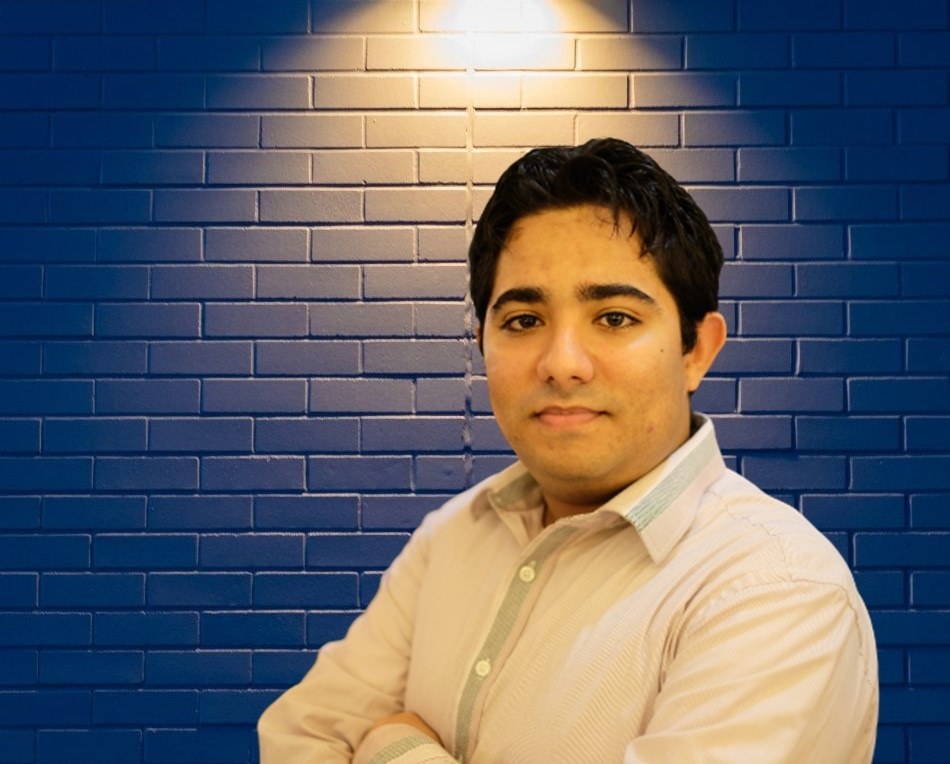 Professor Bruno Gomes seated against a blue brick wall